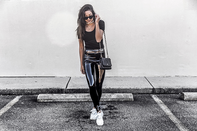 luxury fashion blogger wears a luxury bag, velvet bodysuit and vinyl leather leggings with chunky sneakers